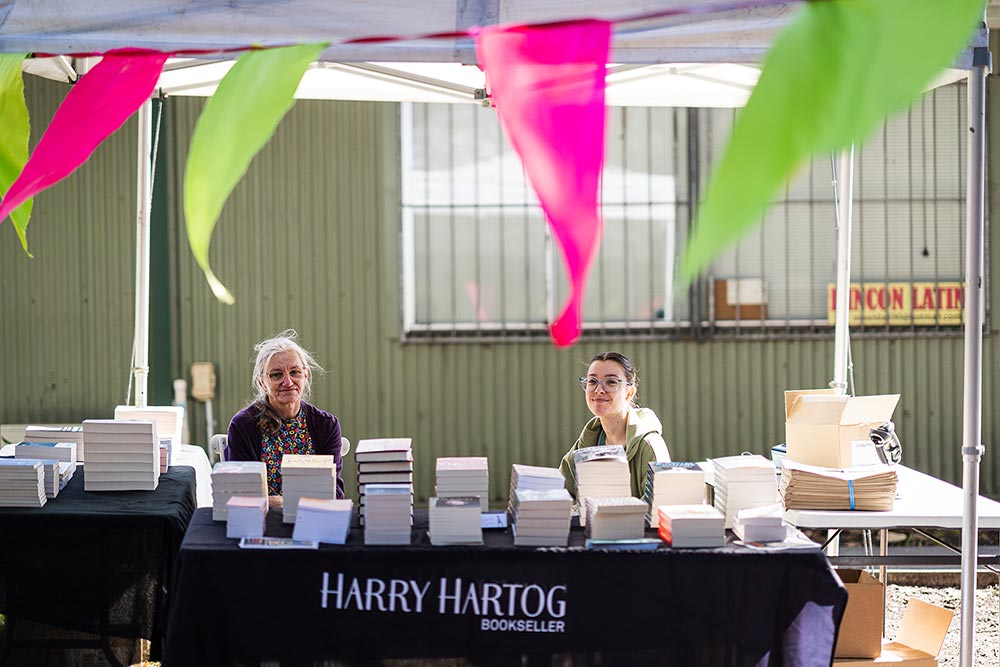 Two women seated behind a table with stacks of books on it